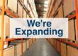 PalStore Warehouse aisle of boxes with text "We're Expanding"